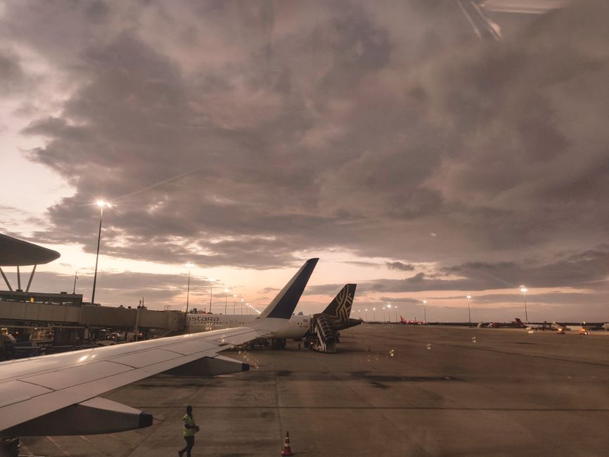 Dramatic sunset view of an airplane wing parked on airport tarmac under cloudy skies.